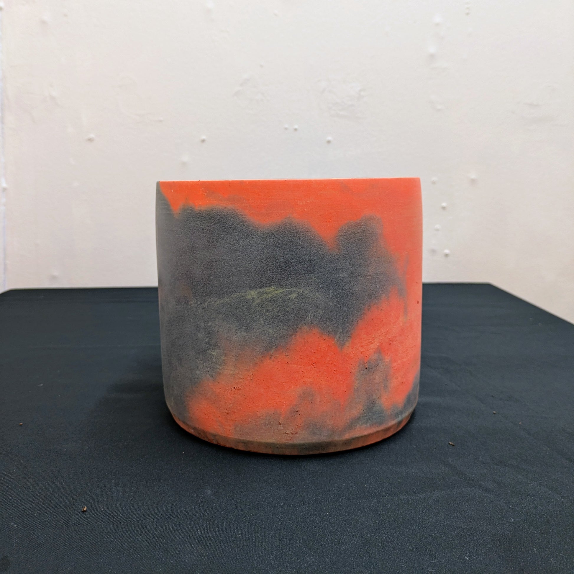 The picture shows a grey and orange marbled concrete plant pot, this a front facing view showing the colour split between orange and grey.
