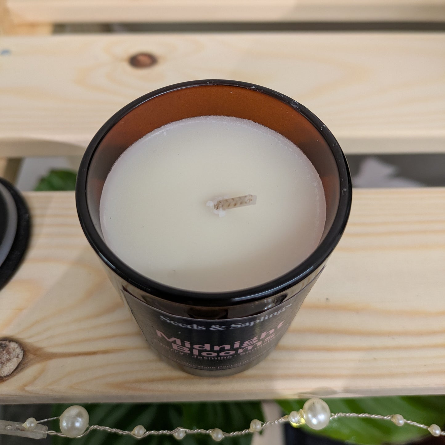 The image shows a top-down shot of an amber jar candle showing the wax surface and wick.