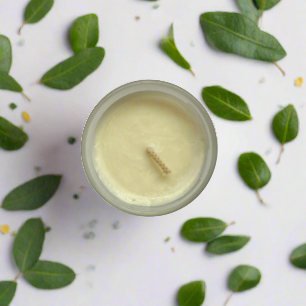 Top down view of the surface of the candle and the wick. The table underneath the candle is covered in eucalyptus leaves.